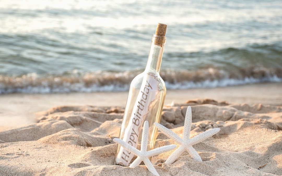 happy birthday beach party message inside bottle next to starfish on the beach