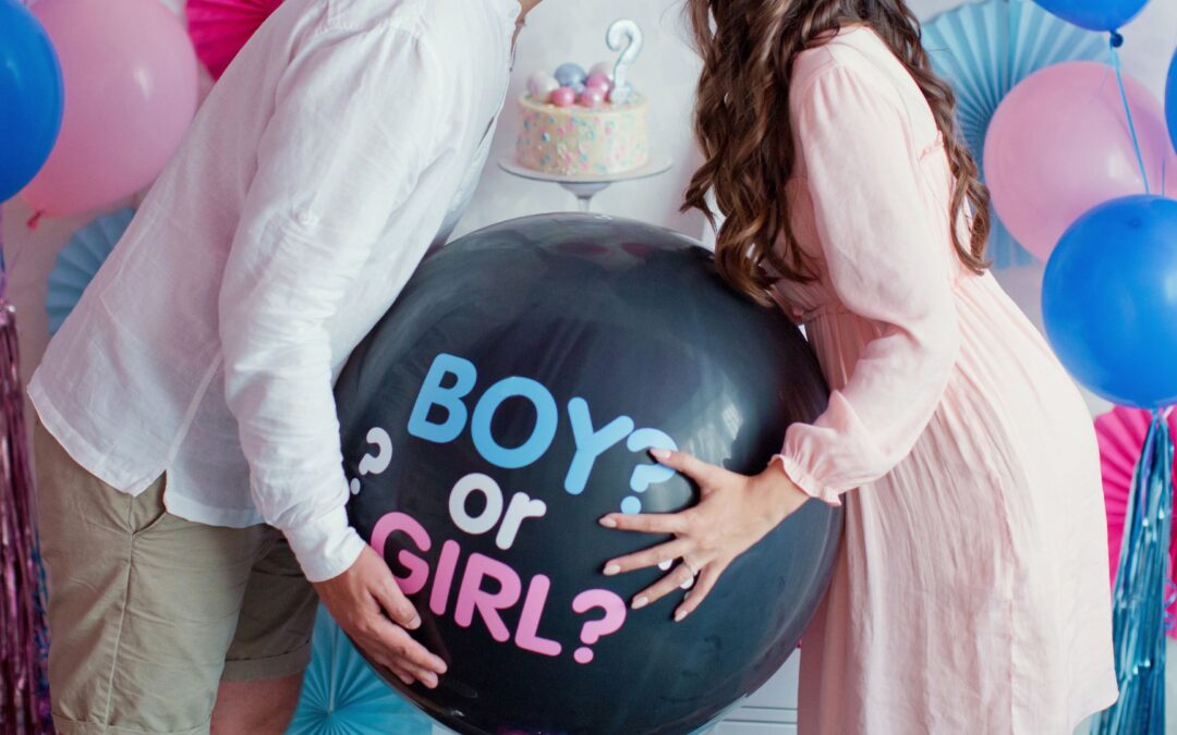 new parents share a kiss over a balloon that reads "Boy or Girl?" at a gender reveal party